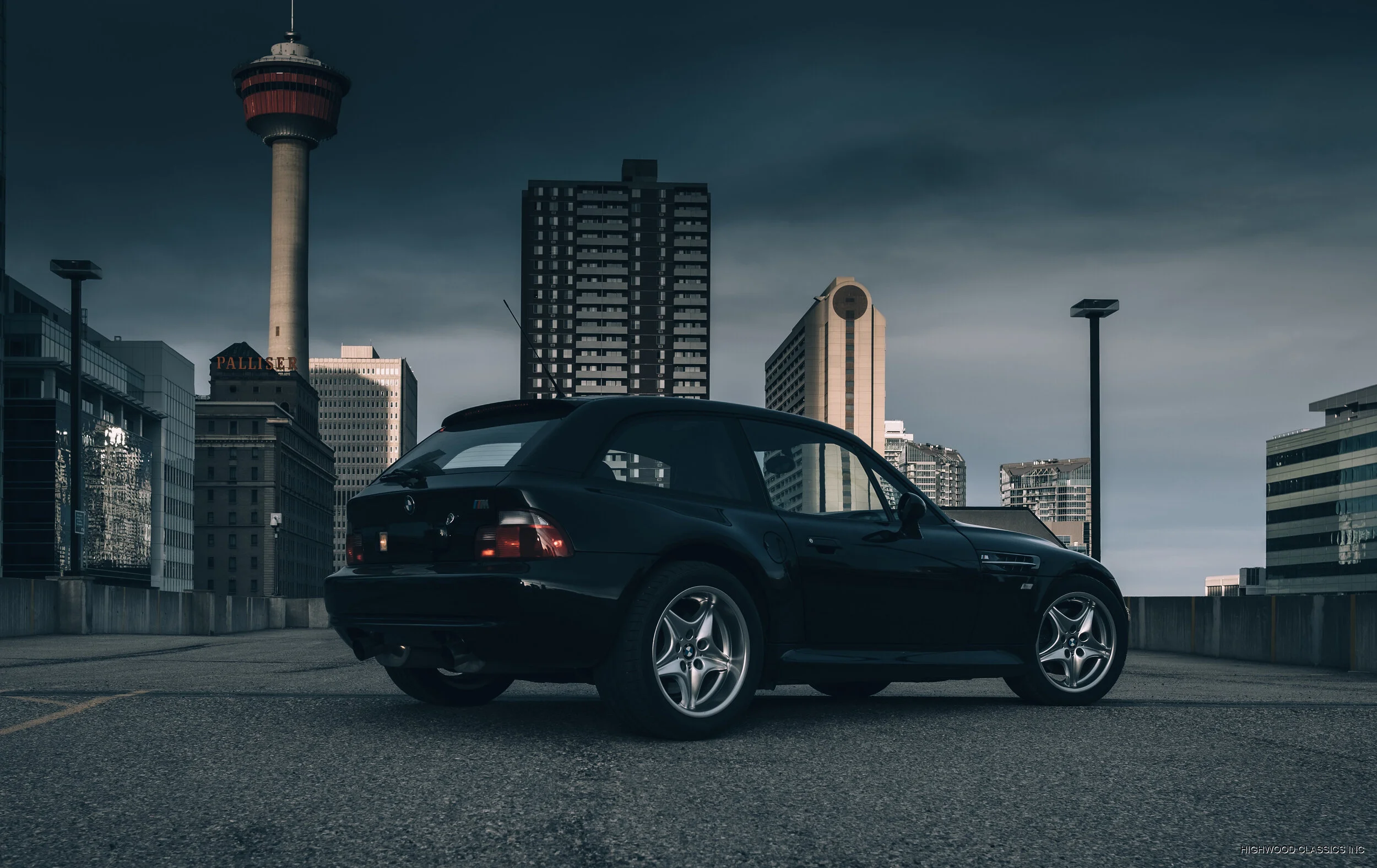 A dark classic coupe parked against a city skyline.